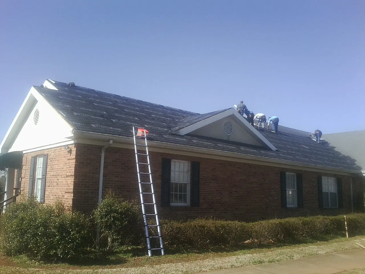 Crew tearing shingles off a brick ranch roof with a ladder set — Emergency Roof Repair work by our crew in Liverpool