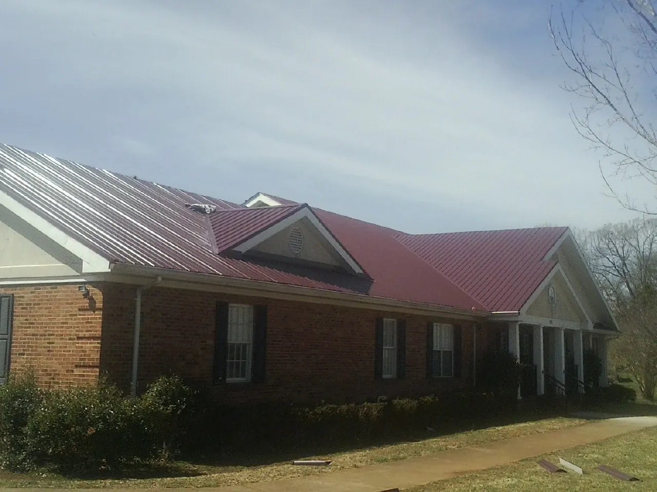 Red metal roof with gabled entries on a long brick building, from a Hail Damage Roof Repair job in Liverpool