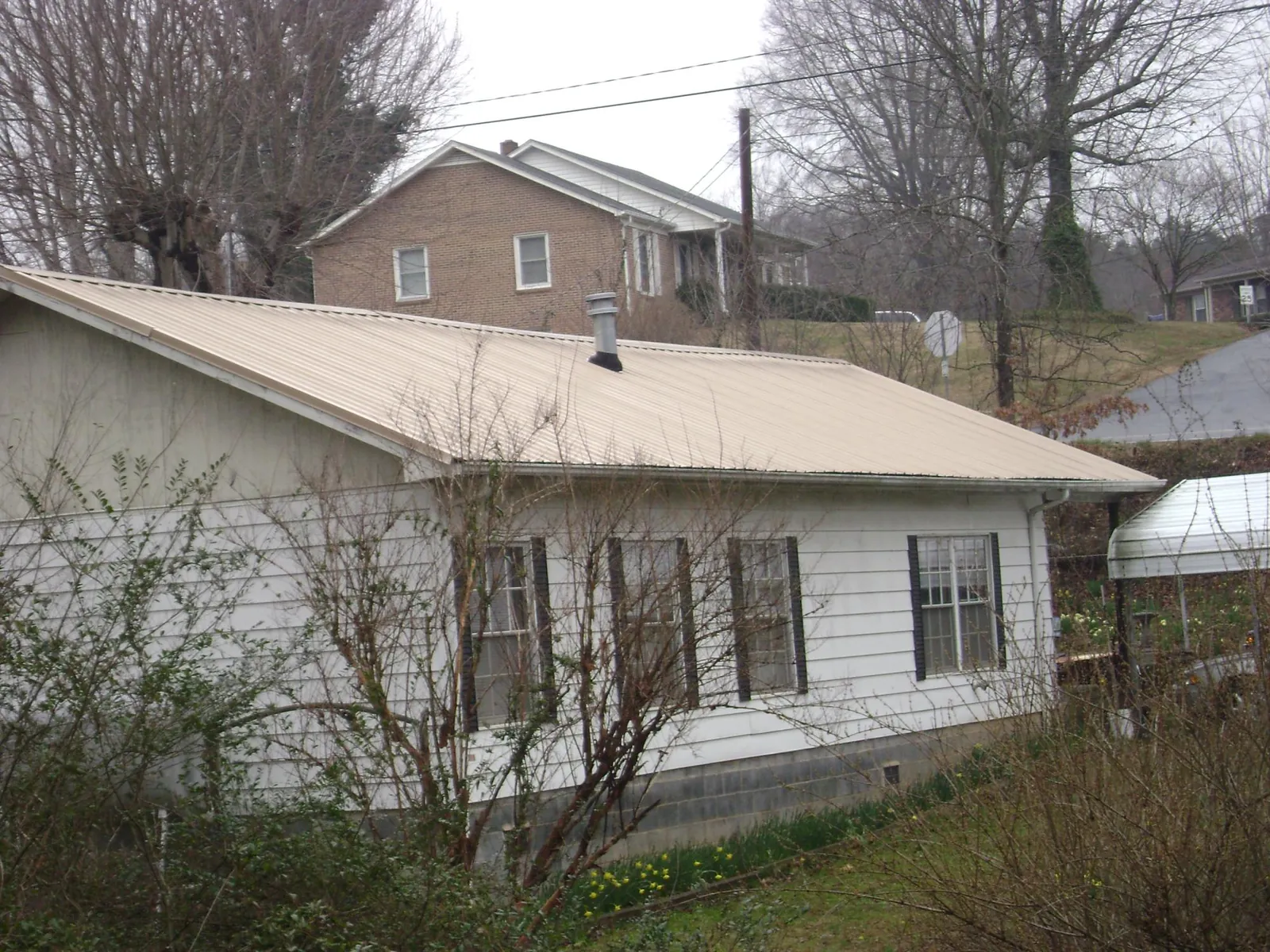 Tan metal roof on a white sided house set into a hillside — Commercial Roofing by Roofing Brothers in Liverpool